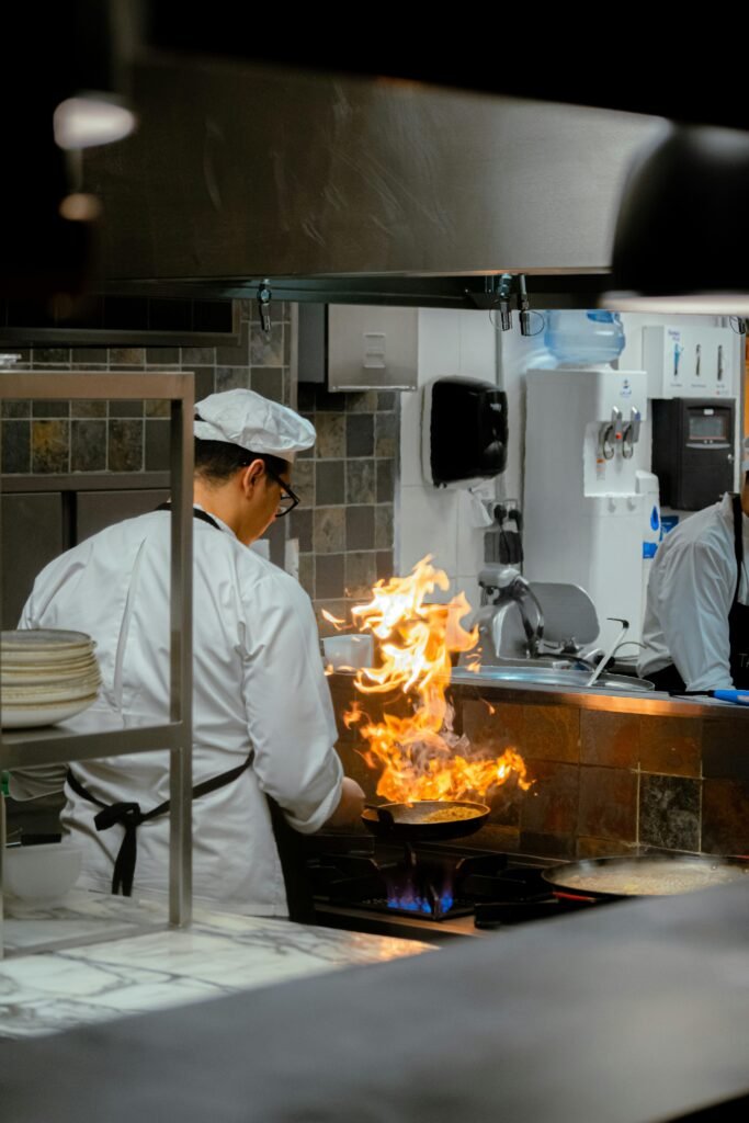 A chef skillfully handles a flaming pan in a commercial kitchen, showcasing culinary expertise.